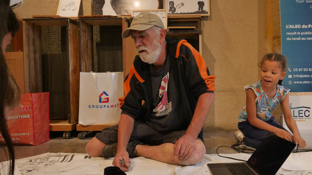 Un bénévole de l’association Bouche à Oreille (BAO) choisit les dessins avec les enfants du P'tit Lab. Accrochage de l'exposition Portraits sonores, le 6 juillet au Cloître des Récollets à Metz | Photo et graphisme BORNYBUZZ / Aurélien ZANN